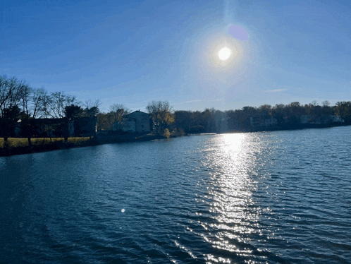 the sun shines brightly over a lake with houses in the background