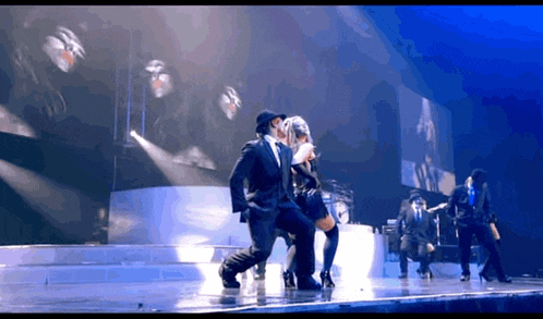 a man in a suit is dancing with a woman in a hat on a stage