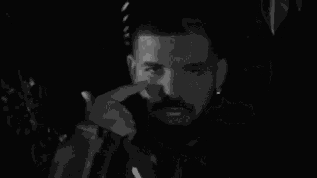 a black and white photo of a man with a beard covering his face with his hands .