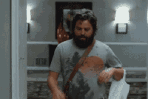 a man with a beard is standing in a hallway holding a purse