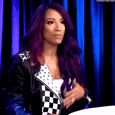 a woman with purple hair is wearing a black and white checkered jacket and a white tank top .