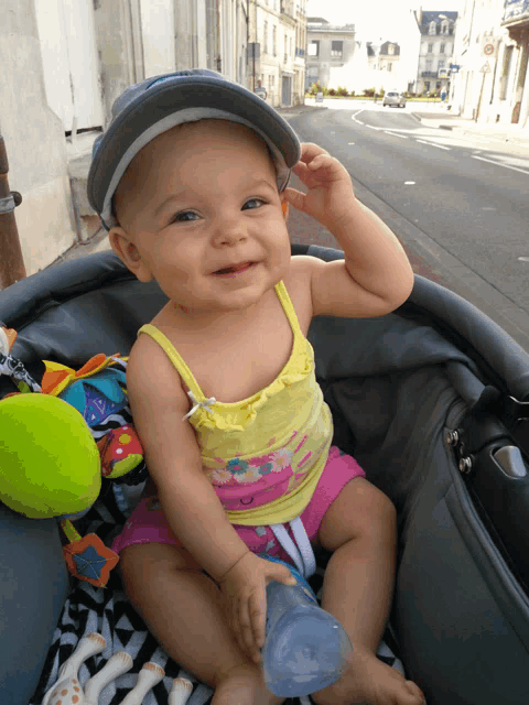 a baby is sitting in a stroller holding a bottle and wearing a hat