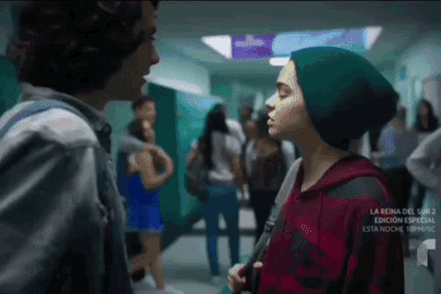 a man and a woman are standing in a hallway with a sign that says la reina del sur 2 on it