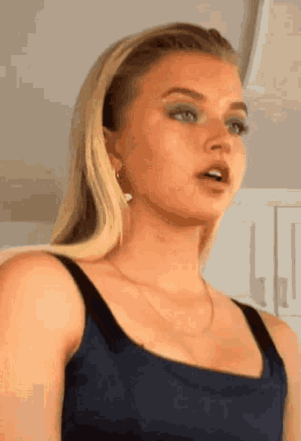 a close up of a woman wearing a blue tank top and a necklace .
