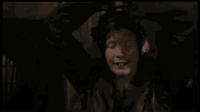 a woman wearing a black hat and a black jacket is sitting in a dark room .