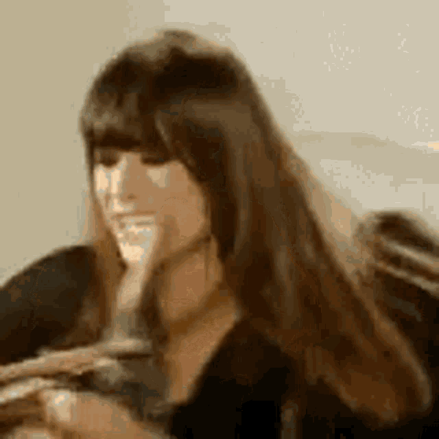 a woman with long hair and bangs is smiling and holding a bottle of wine .