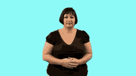 a woman in a black shirt is standing in front of a blue background and making a hand gesture .