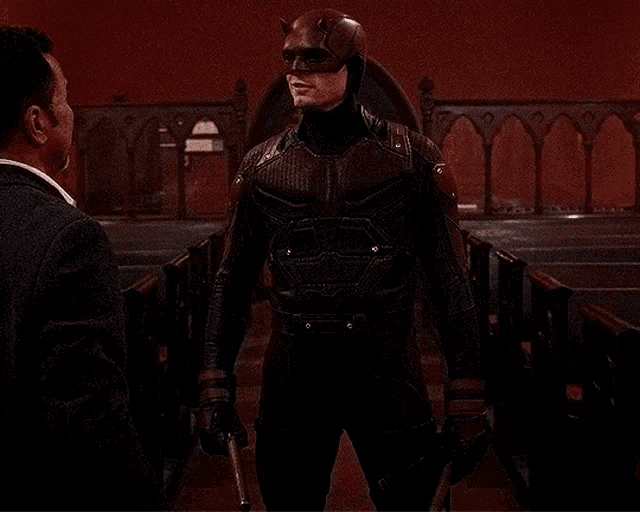 a man in a daredevil costume is talking to another man in a church