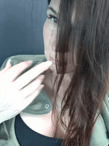a woman covering her face with her hair while wearing a black shirt and a green jacket