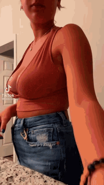 a woman wearing a crop top and jeans is standing in front of a counter .