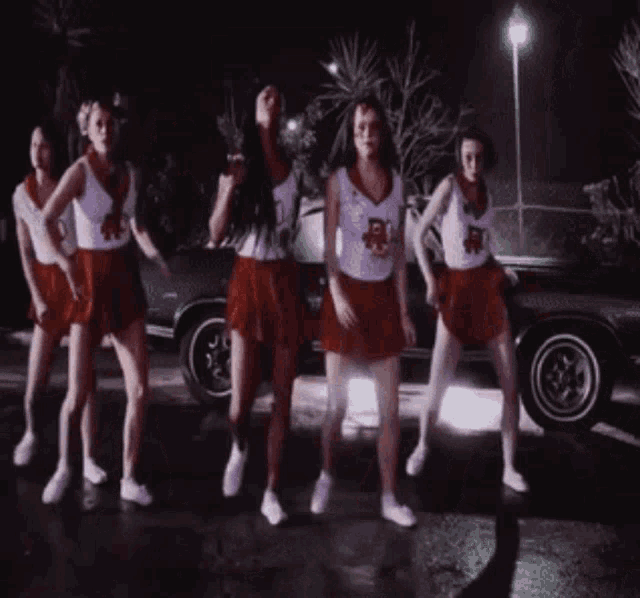 a group of cheerleaders are standing in front of a car wearing shorts with the letter r on them