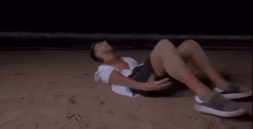 a shirtless man is sitting on a sandy beach at night .