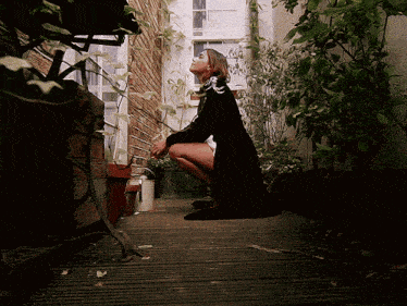 a woman in a black coat squatting on a wooden deck