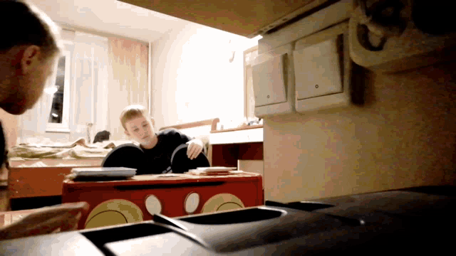 a boy sits at a desk in front of a red mickey mouse toy box