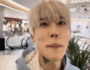 a young man with blonde hair and a tattoo on his neck is looking at the camera in a mall .