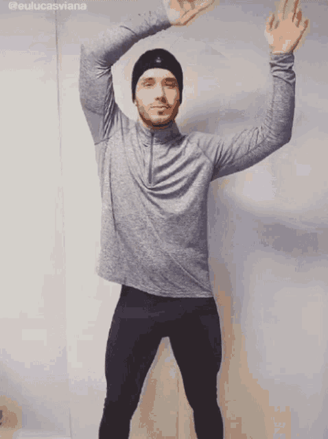 a man in a gray shirt and black pants is dancing with his hands in the air .