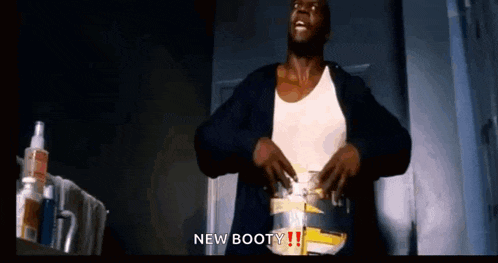 a man in a white tank top is standing in a dark room with his hands on his hips and says `` new booty '' .