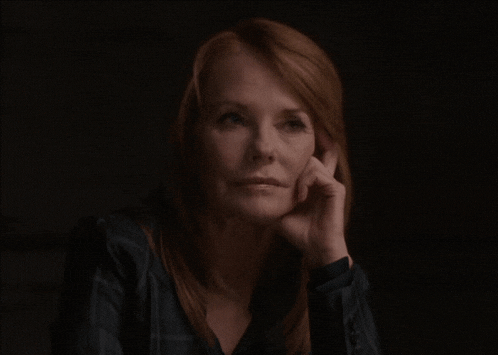 a woman with red hair holds her hand to her face in a dark room