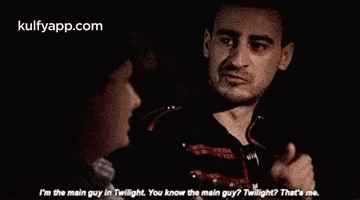 two men are talking to each other in a dark room and one of them is giving a thumbs up .