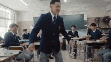 a man in a suit and tie is dancing in a classroom while other students sit at desks .