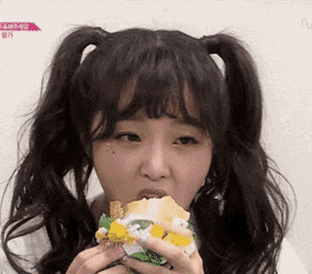 a girl with pigtails is eating a sandwich with a yellow topping