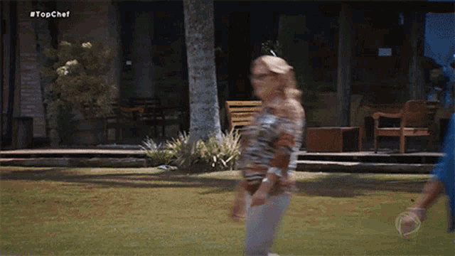 a blurred image of a woman walking in front of a house with the hashtag #topchef on the bottom
