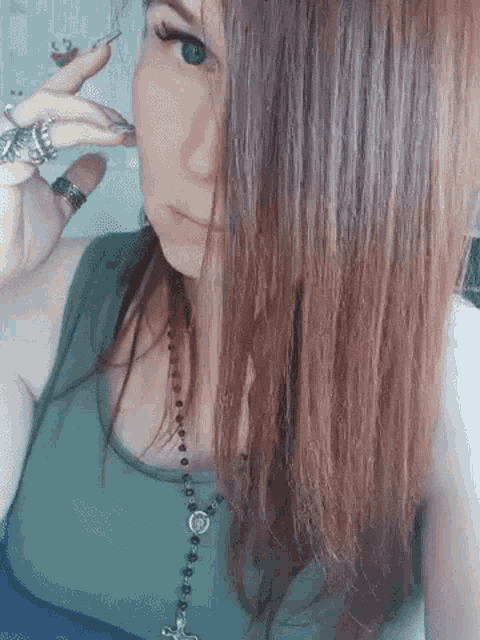 a woman with long red hair wearing a green tank top and a rosary necklace