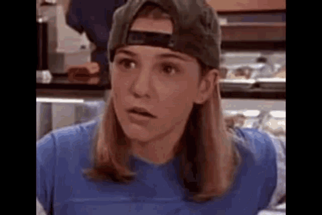 a woman wearing a baseball cap and a blue shirt is making a surprised face .