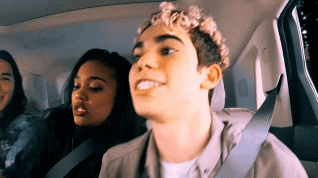 a young man with curly hair is sitting in the back seat of a car with two women .