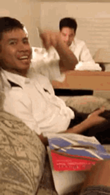 a man in a white shirt is sitting on a couch and smiling