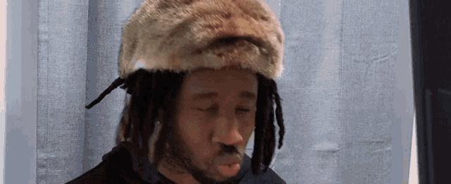 a man with dreadlocks is wearing a furry hat