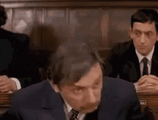 a man in a suit and tie is sitting at a table in front of a group of men .