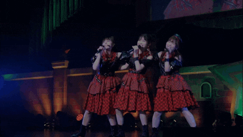three girls singing into microphones on a stage with a star in the background