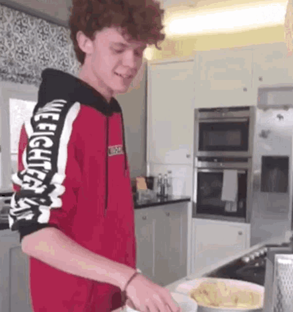 a young man in a red hoodie is cooking food in a kitchen .