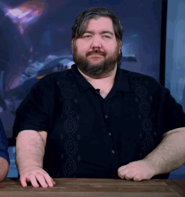 a man with a beard is sitting at a table with his hands on his hips