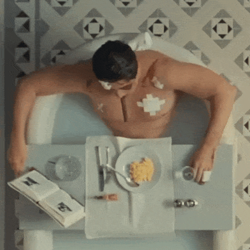 a man is laying in a bathtub with a plate of food and a book