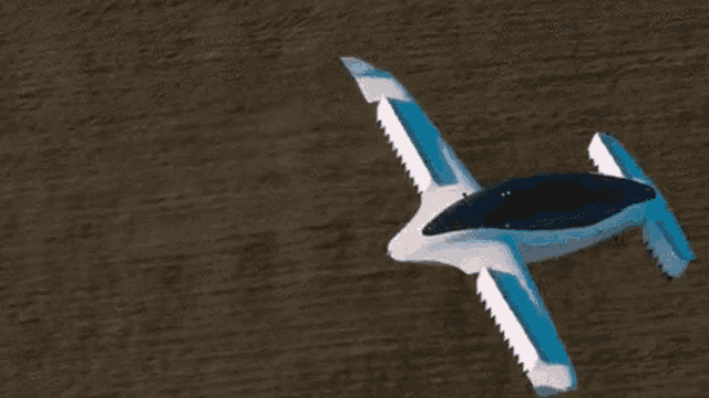 a small white and blue airplane is flying over a dirt field