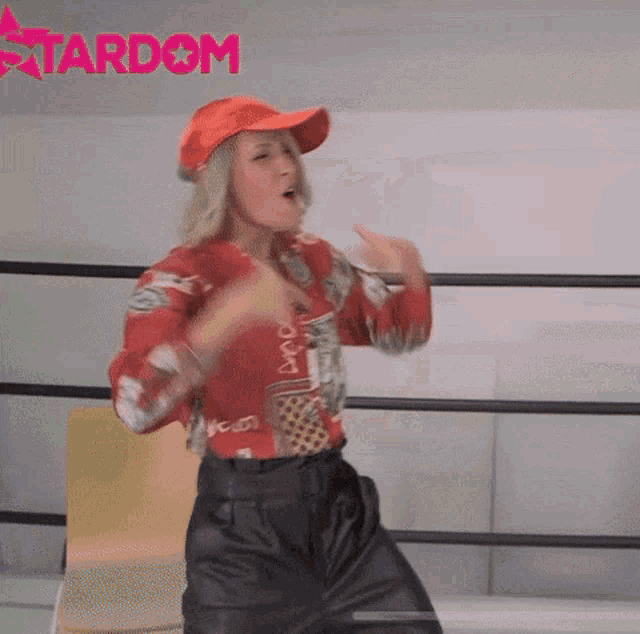 a woman wearing a red hat and black shorts is dancing in a ring with the word stardom in the background .