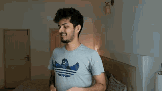 a man wearing a grey adidas t-shirt is standing in front of a bed