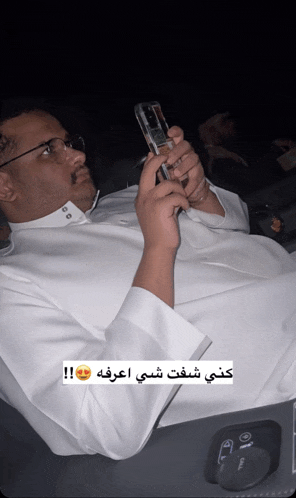 a man in a white robe is holding a cell phone with arabic writing on it