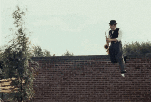 a man in a hat is playing a saxophone while jumping over a brick wall