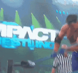 a referee stands in front of a large impact wrestling sign