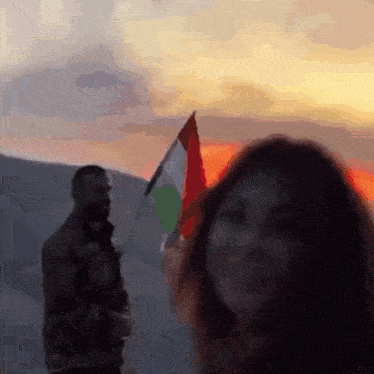 a man and a woman are standing next to each other with a flag in the background .