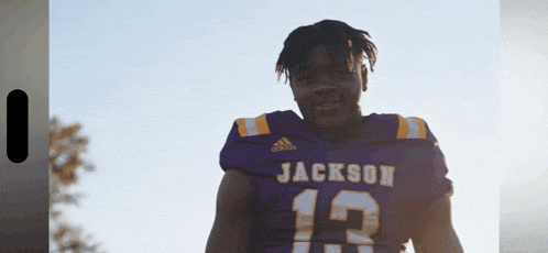 a man wearing a jackson 13 jersey stands in front of a blue sky