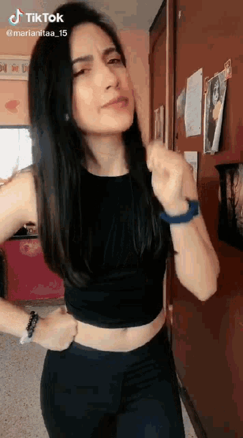 a woman in a black crop top and black pants is standing in front of a wall .