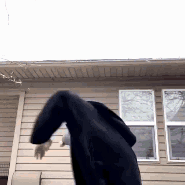 a person in a black coat is standing in front of a house with windows