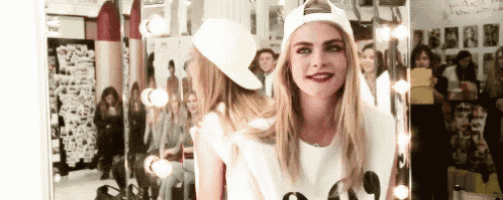 a woman wearing a baseball cap is standing in front of a mirror and smiling