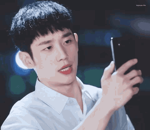 a young man in a white shirt is looking at his cell phone .