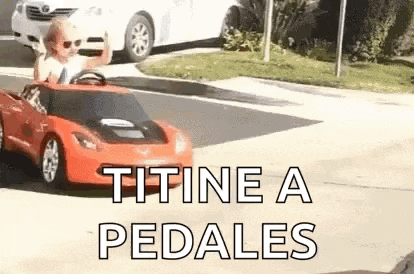 a little boy is driving a red toy car down the street .
