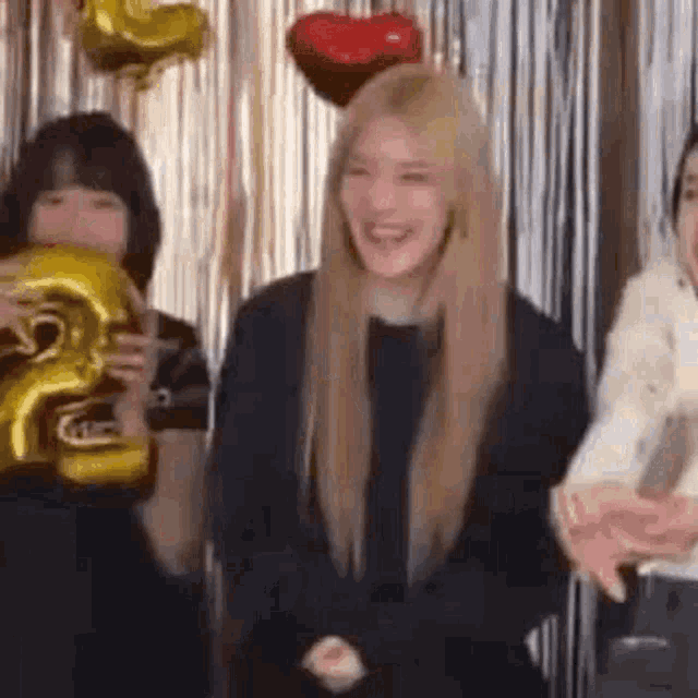 a woman is laughing while holding a number 2 balloon in front of a group of people .